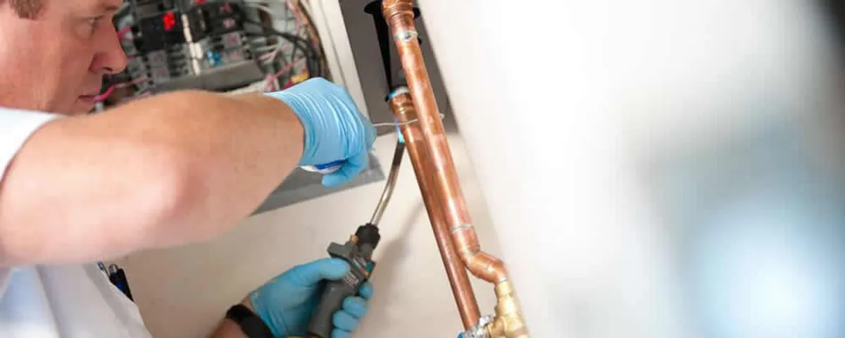 Water heater repair technician testing copper pipe connections and controls in Durham, NC